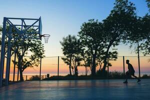 zwart Mens aan het doen sport, spelen basketbal Aan zonsopkomst, silhouet foto