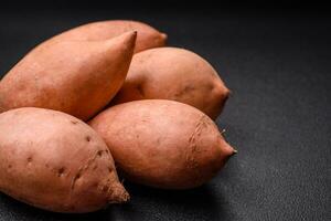 vers groot roze zoet aardappel knollen met tomaten en specerijen Aan een donker achtergrond foto