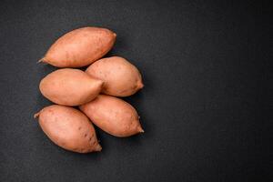 vers groot roze zoet aardappel knollen met tomaten en specerijen Aan een donker achtergrond foto