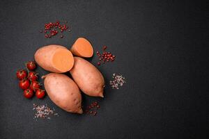 vers groot roze zoet aardappel knollen met tomaten en specerijen Aan een donker achtergrond foto