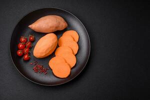 vers groot roze zoet aardappel knollen met tomaten en specerijen Aan een donker achtergrond foto