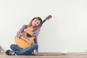 mooie vrouw zit met haar gitaar gelukkig zittend op de houten foto