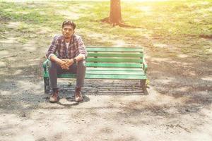 jonge hipster man zit op een houten bankje in het park. foto