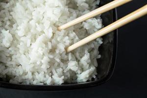 kom met gekookte rijst op zwarte achtergrond. Aziatisch eten foto