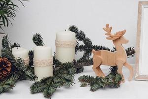 drie kerstkaarsen, kerstballen, tak van dennen en houten herten foto