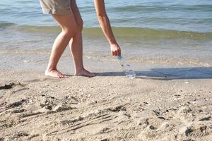 jonge vrouw haalt gebruikte plastic fles op van strand naar schone kust foto