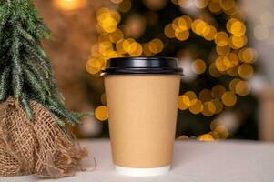 een beschikbaar koffie kop met een deksel Aan de achtergrond van een Kerstmis boom. plaats voor reclame foto