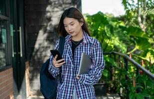 jong gelukkig tiener leerling Holding mobiel telefoon en laptop vervelend rugzak, onderwijs en aan het leren online terug naar school- concept. foto