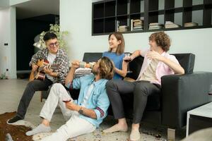 multi-etnisch groep van vrienden hebben pret spelen gitaar en het zingen samen Bij huis foto