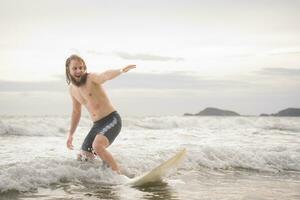 jong Mens surfing Aan de strand hebben pret en balanceren Aan de surfboard foto