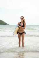 portret van glimlachen jong vrouw staand met surfboard Bij de strand foto