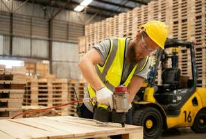 jong arbeiders werken in een houtbewerking fabriek, gebruik makend van een spijkeren machine naar monteren houten pallets foto