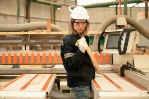 jong vrouw arbeider werk in een houtbewerking fabriek, werken met hout zagen en snijdend machines naar produceren houten lakens voor maken pallets foto