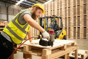 jong arbeiders werken in een houtbewerking fabriek, gebruik makend van een spijkeren machine naar monteren houten pallets foto