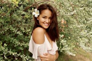 bevallig Aziatisch vrouw met perfect huid en hibiscus bloem in haren poseren over- hout muur en tropisch planten. zomer mode portret. foto