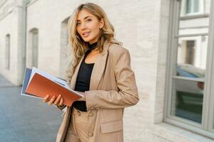 succesvol blond bedrijf vrouw poseren in elegant pak buitenshuis. Holding bontwerper catalogi. foto