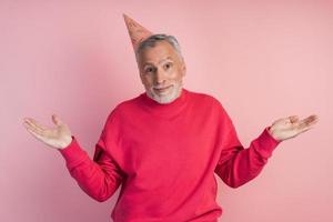 senior man met een feestelijke hoed op een roze achtergrond foto