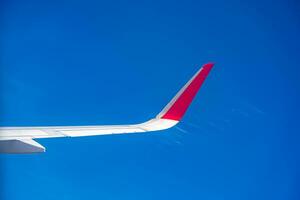 visie van vliegtuig venster met blauw lucht en wit wolken. rood tip foto