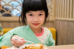 schattig weinig Aziatisch kind meisje aan het eten voedsel foto