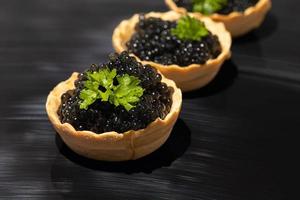 zwarte kaviaar in taartjes op een donkere achtergrond. gezond voedselconcept. foto