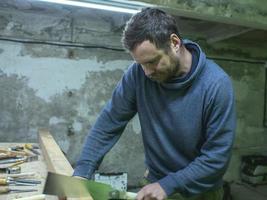 houtbewerker met een baard die een houten balk zaagt met een handzaag foto