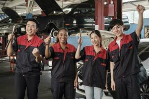 multiraciaal professioneel monteur arbeiders team na werk vieren automotive reparatie jobs succes, hand- verhoogt met vaststelling gereedschap met vrolijk glimlacht en kijken Bij camera Bij een onderhoud auto garage. foto