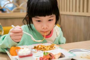 schattig weinig Aziatisch kind meisje aan het eten voedsel foto