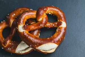 twee eigengemaakt vers gebakken zacht pretzels Aan zwart achtergrond. traditioneel Beiers zoute krakeling voor Oktoberfest. top visie, kopiëren ruimte foto