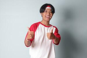 portret van aantrekkelijk Aziatisch Mens in t-shirt met rood en wit lint Aan hoofd, tonen mooi zo baan hand- gebaar met duimen omhoog. geïsoleerd beeld Aan grijs achtergrond foto
