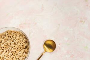 heerlijk honing cheerios ontbijtgranen in een kom en gouden lepel Aan roze achtergrond. top visie, kopiëren ruimte foto