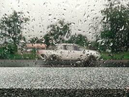 leeg steen plank met regen vallend Aan wazig straat glas met auto's voor weergeven regenachtig seizoen producten. foto