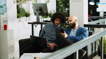 twee medewerkers vergelijken aantekeningen in kantoor, herzien online bedrijf gegevens Aan laptop en tablet. mensen planning nieuw presentatie voor uitvoerend bord ontmoeting, gebruik makend van officieel papieren. statief schot. foto