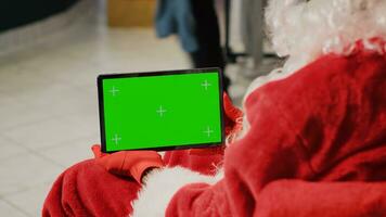 werknemer in Kerstmis overladen kleding op te slaan gekleed net zo de kerstman claus Holding groen scherm tablet, instelling omhoog website kleding Lidwoord, invoeren promotionele Kerstmis aanbiedingen online foto