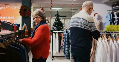 tachtigjarige klanten browsen door kleding rekken in feestelijk overladen mode winkel gedurende winter vakantie seizoen. senior paar gelukkig na vinden kleurrijk blazers naar geschenk Bij Kerstmis familie bijeenkomst foto