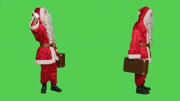 persoon met aktentas in rood pak, aan het wachten voor iets terwijl hij draagt koffer staand over- vol lichaam groene scherm. de kerstman claus karakter met bagage gedurende Kerstmis viering. foto