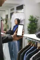 kleding op te slaan klant Mens hand- Holding smartphone met blanco wit scherm model, controle kleding Aan winkel website. boodschappen doen winkelcentrum cliënt gebruik makend van mobiel telefoon met leeg touch screen foto