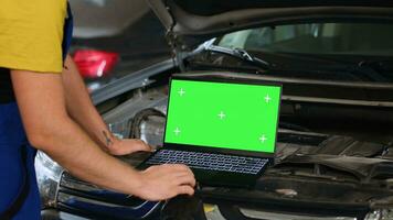 ingenieur gebruik makend van groen scherm laptop in auto onderhoud naar bestellen nieuw onderdelen voor beschadigd voertuig. dichtbij omhoog schot van deskundige gebruik makend van chroma sleutel apparaat naar kijken online voor componenten naar vervangen oud degenen foto