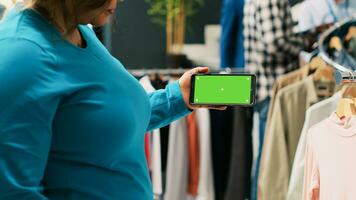 Afrikaanse Amerikaans vrouw analyseren telefoon met groene scherm sjabloon, op zoek Bij geïsoleerd Scherm in modern boetiek. elegant klant boodschappen doen voor modieus kleding in kleding op te slaan. mode concept foto