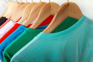 mode t-shirt Aan kleding rek - detailopname van helder kleurrijk kast Aan houten hangers in op te slaan kast. foto
