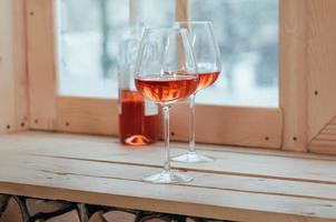een fles rose wijn en twee gevulde glazen op een vensterbank