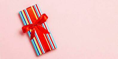 verpakt Kerstmis of andere vakantie handgemaakt Cadeau in papier met rood lint Aan roze achtergrond. Cadeau doos, decoratie van geschenk Aan gekleurde tafel, top visie met kopiëren ruimte foto