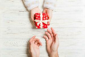 top visie van Holding een geschenk in vrouw en mannetje handen Aan houten achtergrond. vrouw en Mens geven en te ontvangen een Geschenk. dichtbij omhoog van tijd voor vakantie concept foto