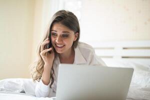 gelukkige mooie vrouw die aan laptop op het bed in het huis werkt foto