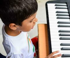 Aziatisch jongen spelen de synthesizer of piano. schattig weinig kind aan het leren hoe naar Speel piano. kind handen Aan de toetsenbord binnen. foto