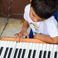 Aziatisch jongen spelen de synthesizer of piano. schattig weinig kind aan het leren hoe naar Speel piano. kind handen Aan de toetsenbord binnen. foto