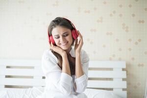 mooie vrouw die 's ochtends muziek luistert terwijl ze thuis op bed zit foto