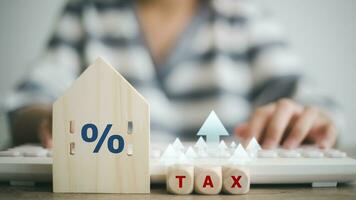 de concept van betalen staat eigendom belasting. een zakenvrouw met een houten huis met een procent teken en pijl omhoog huis staat. foto