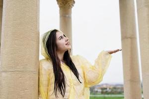 mooie donkerbruine vrouw in gele regenjas die buiten regen vangt foto