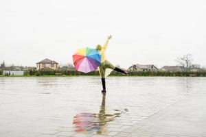 mooie donkerbruine vrouw die kleurrijke paraplu houdt die in de regen danst foto