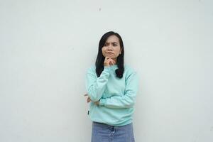 portret Indonesisch mooi vrouw vervelend licht blauw trui met denken gebaar geïsoleerd Aan wit achtergrond foto